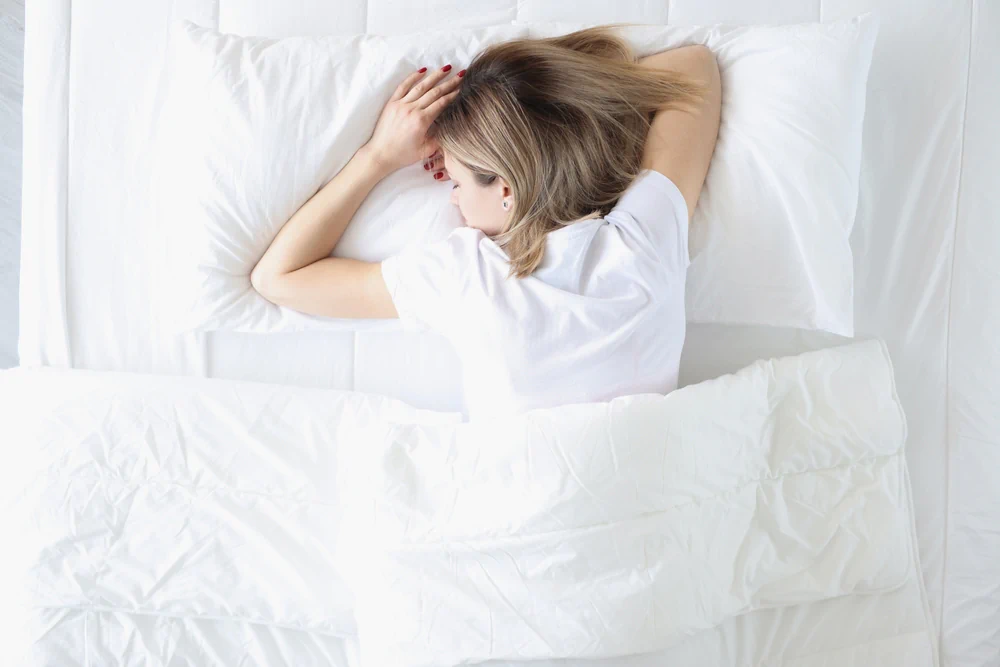 Woman sleeping on her stomach in a white bed