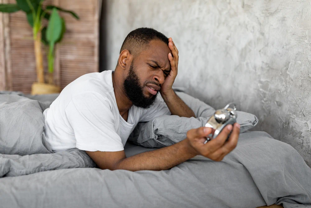 Man in bed looking shocked at his alarm clock