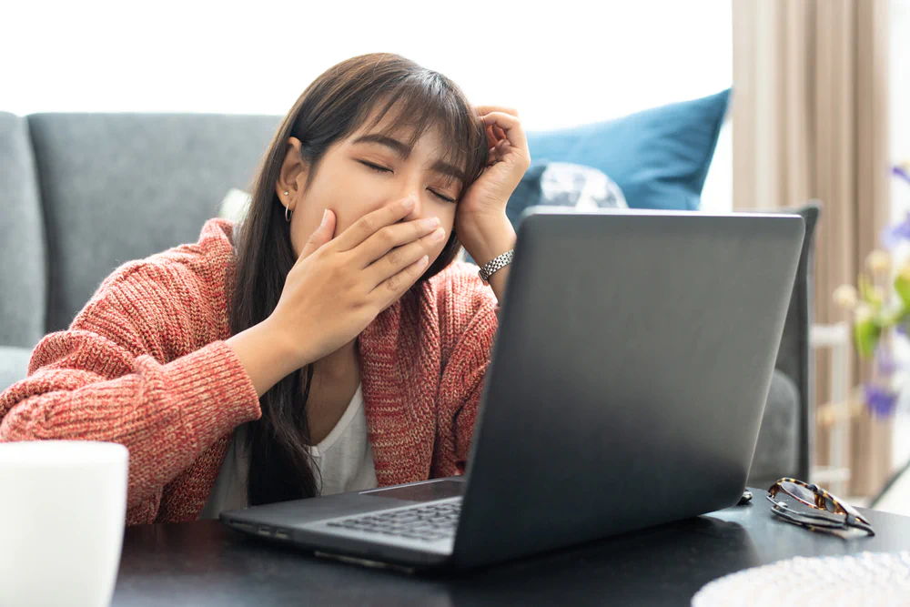 Young woman yawning in front of her computer daytime drowsiness