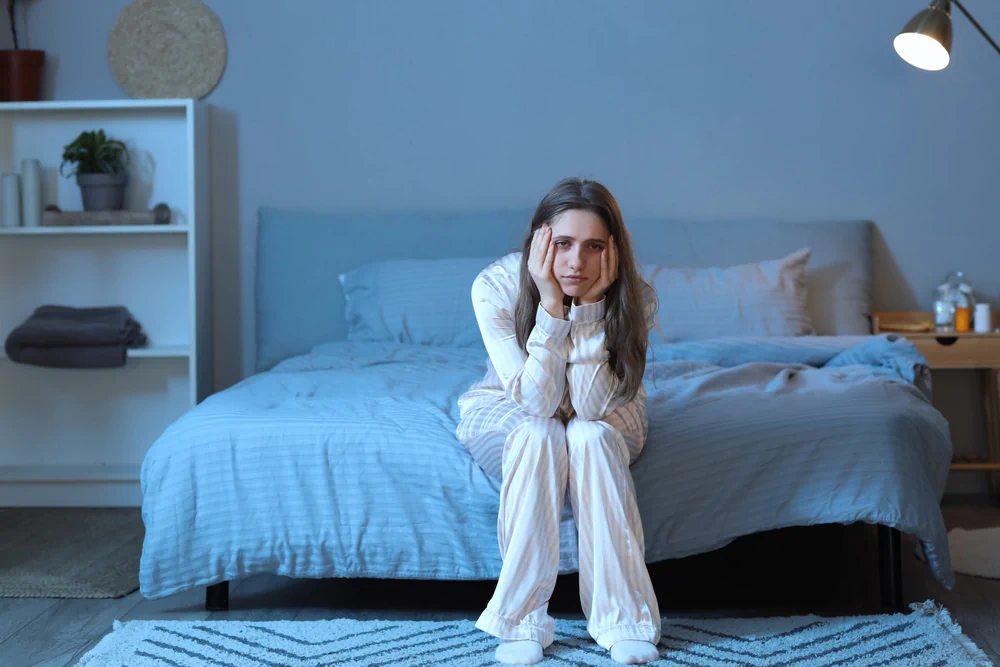 Stressed young woman suffering from winter insomnia in bedroom at night